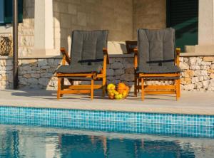 波斯蒂拉Holiday home Blato的游泳池畔的两把椅子和一碗水果