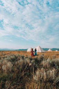 艾兰帕克Yellowstone Glamping的两人坐在帐篷旁边的田野里