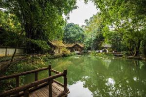 成都Chengdu Ren He Spring Hotel的花园中的池塘,花园内设有木凳