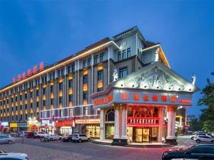 天津Vienna Hotel Tianjin Huaming的街道上一座大型建筑,停车场内有车辆停放