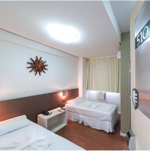 迪维诺波利斯Excellence Comfort Hotel的酒店客房设有两张床和墙上的时钟。