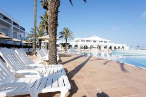 埃斯卡纳特尔Grupotel Mar de Menorca的游泳池旁的一排白色躺椅