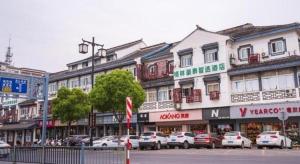 苏州GreenTree Inn Express Suzhou Luzhi Ancient Town Scenic Area Xiaoshi Road的一条城市街道,汽车停在建筑前