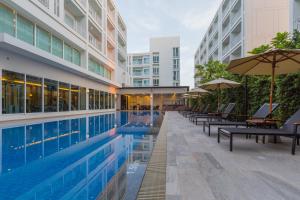 Si Maha Phot巴真武里坎纳瑞304酒店的大楼旁的游泳池配有长椅和遮阳伞