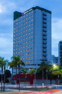 维多利亚普拉亚都坎托司丽普酒店的一座高大的建筑,前面有棕榈树