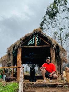 蒙纳Roamrustic Camp Vattavada的坐在茅草小屋里的人和狗