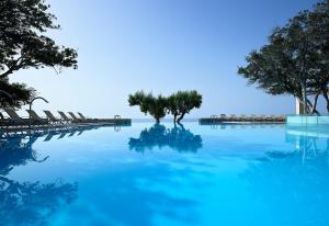 依拉佩特拉卡科斯海湾简易别墅酒店的一个带椅子和树木的蓝色海水游泳池