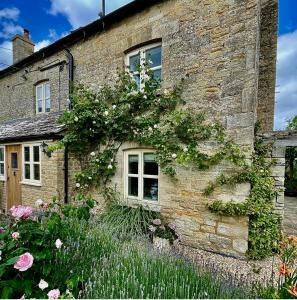 QueningtonCosy Cotswold Cottage with garden Quenington near Bibury的一座古老的石头房子,前面有鲜花