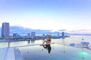 岘港IBIZA Riverfront Da Nang Hotel Powered by ASTON的坐在城市顶部游泳池边的女人