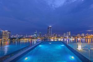 岘港IBIZA Riverfront Da Nang Hotel Powered by ASTON的一座晚上拥有城市天际线的游泳池