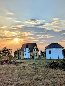 巴加莫约Bagamoyo Home Stay的两座房子在田野,背面是日落