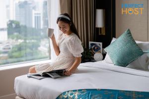 吉隆坡Pavilion Ceylon Hill Suites, Bukit Bintang的坐在床上拿着咖啡杯的年轻女孩