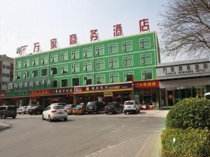 北京Beijing Wanjia Traders Hotel的一座绿色建筑,前面有汽车停放