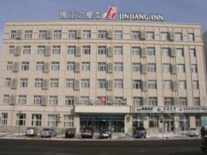 长春Jinjiang Inn Changchun Pepole Square的一座大型建筑,前面有汽车停放