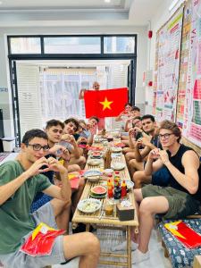 胡志明市ALOHA SAIGON HOSTEL by Local Travel Experts - Newly opened, Less-touristy location, Spacious rooms, Glass shower bathroom, Free breakfast, Quiet alley and Cultural exploration的一群人坐在一张长桌旁,挂着旗帜