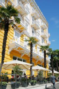 奥帕提亚BRISTOL Hotel Opatija的一座黄色的建筑,里面种有棕榈树,桌子和遮阳伞