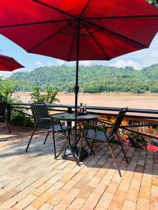 琅勃拉邦Luang Prabang Mekong Charm River View的甲板上红色遮阳伞下的桌椅