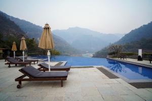 瑞诗凯诗Luxury Aloha Apartments, Rishikesh的山边带椅子和遮阳伞的游泳池