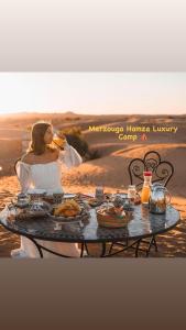 梅尔祖卡Merzouga Hamza Luxury Camp的女人坐在桌子上吃食物