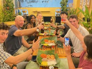 胡志明市Saigon Authentic Hostel - Cozy Rooftop, Family Cooking Experience, FREE Walking Tour, Vietnamese Breakfast & Gym的一群坐在桌边喝啤酒的人