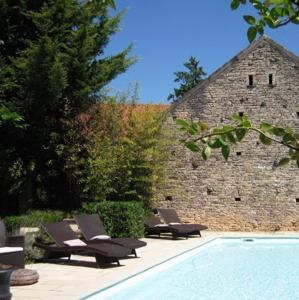 Ladoix Serrigny拉都瓦庄园酒店的两把躺椅和一个游泳池,位于一座石头建筑旁边