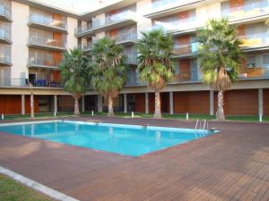 坎布里尔斯Apartamento Playa Esquirol的棕榈树建筑前的游泳池