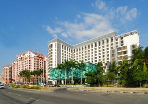哥打京那巴鲁亚庇凯城酒店的一座大型白色建筑,位于一条种有棕榈树的城市街道上