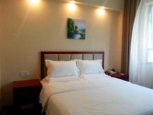 松江格林豪泰上海市松江松东商务酒店的卧室配有一张带白色床单的床,墙上挂着一幅画