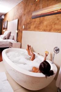 肯普顿帕克African Rock Hotel and Spa的躺在浴缸里的女人,喝一杯葡萄酒