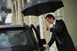 伯尔尼Hotel Schweizerhof Bern & Spa的拿着一把伞的男人,坐在汽车旁边