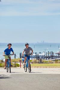 罗特内斯特岛Stay Rottnest的两个人骑着自行车沿着靠近大海的公路行驶