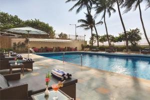 孟买Ramada Plaza By Wyndham Palm Grove的一个带桌椅的游泳池,棕榈树