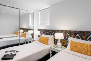 墨尔本Oaks Melbourne South Yarra Suites的一间卧室设有两张床和两张带台灯的桌子。