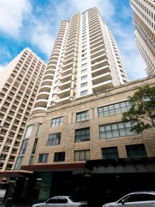 悉尼Oaks Sydney Castlereagh Suites的一座高大的白色建筑,前面有汽车停放