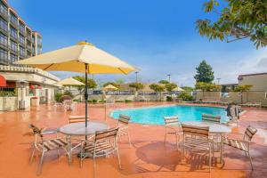 奥克兰奥克兰机场行政酒店的游泳池旁配有遮阳伞的桌椅
