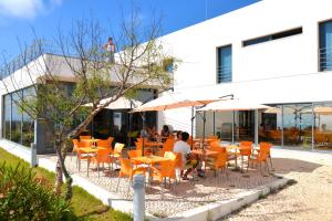 阿尔热祖尔HI Arrifana Destination Hostel的一间设有橙色桌椅的餐厅,一名男子站在一座建筑的顶部