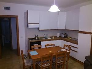 吉诺萨滨海Apartment C的一间带木桌和椅子的厨房和一间带白色橱柜的厨房