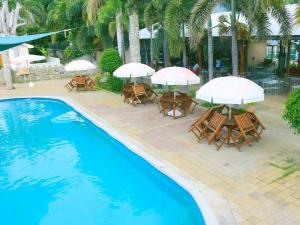 帝力帝汶酒店的一组桌椅,在游泳池旁边配有遮阳伞