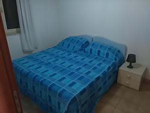 吉诺萨滨海Apartment C的一张蓝色的床,房间有一个灯,放在床头柜上