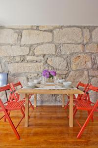 波尔图Porto Sé Apartamentos的一张木桌,配有两张红色椅子和石墙