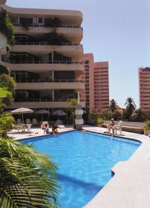 阿卡普尔科Hotel Suites Jazmín Acapulco的一座游泳池,里面的人坐在大楼前的椅子上