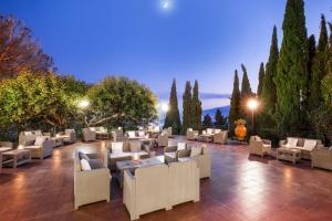 陶尔米纳迪奥多罗别墅酒店的庭院配有白色的桌椅和树木