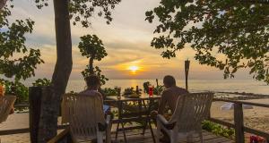 俊穆岛裕姆岛度假村的两人坐在海滩的桌子上,欣赏日落