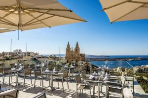 梅利哈玛丽蒂姆马耳他酒店的阳台餐厅,配有桌子和遮阳伞