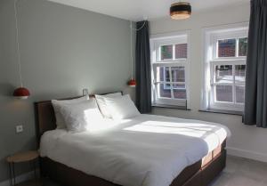 登博斯Boutique Hotel Nieuw Uilenburg的一间卧室配有一张带白色床单的床和两个窗户。