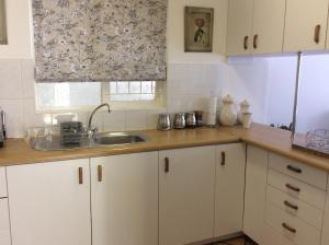 开普敦On Broadwalk Cottage的厨房配有白色橱柜、水槽和窗户。