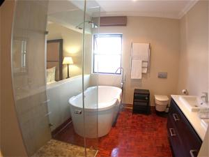 约翰内斯堡Rosebank Lodge Guesthouse by Claires的带浴缸和玻璃淋浴间的浴室。