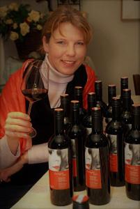 艾森斯塔特Weinhaus Eva-Maria Wagner的一位女士拿着一杯葡萄酒,紧挨着一束葡萄酒瓶