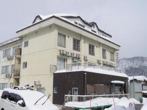 野沢卡多瓦几馆酒店的一座有雪盖的建筑,前面有一辆汽车停放