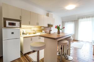 塞格德Aqualiget-Apartmanház的厨房配有白色橱柜和带凳子的台面